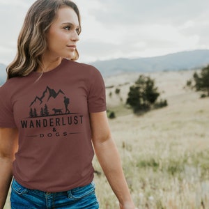 May include: A maroon t-shirt with a graphic of mountains, a person hiking, and a dog. The text "Wanderlust & Dogs" is printed below the graphic.