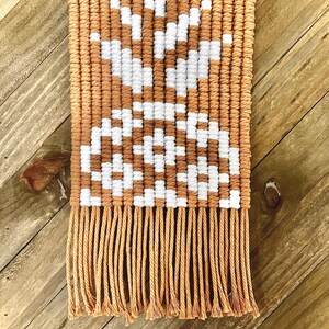 May include: Tan and white macrame wall hanging with a geometric design and fringe.
