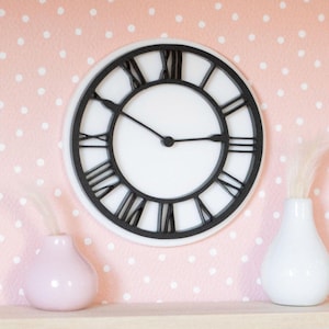 May include: A white clock with black Roman numerals and hands hangs on a pink polka dot wall. Two small vases, one pink and one white, sit on a white shelf below the clock. The clock and vases create a decorative display.
