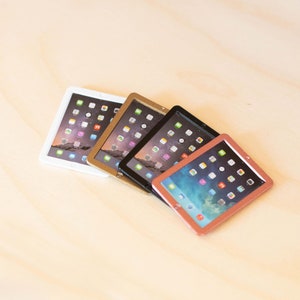May include: Four miniature tablet computers in different colors: white, gold, black, and rose gold. Each tablet has a screen displaying a grid of colorful icons.