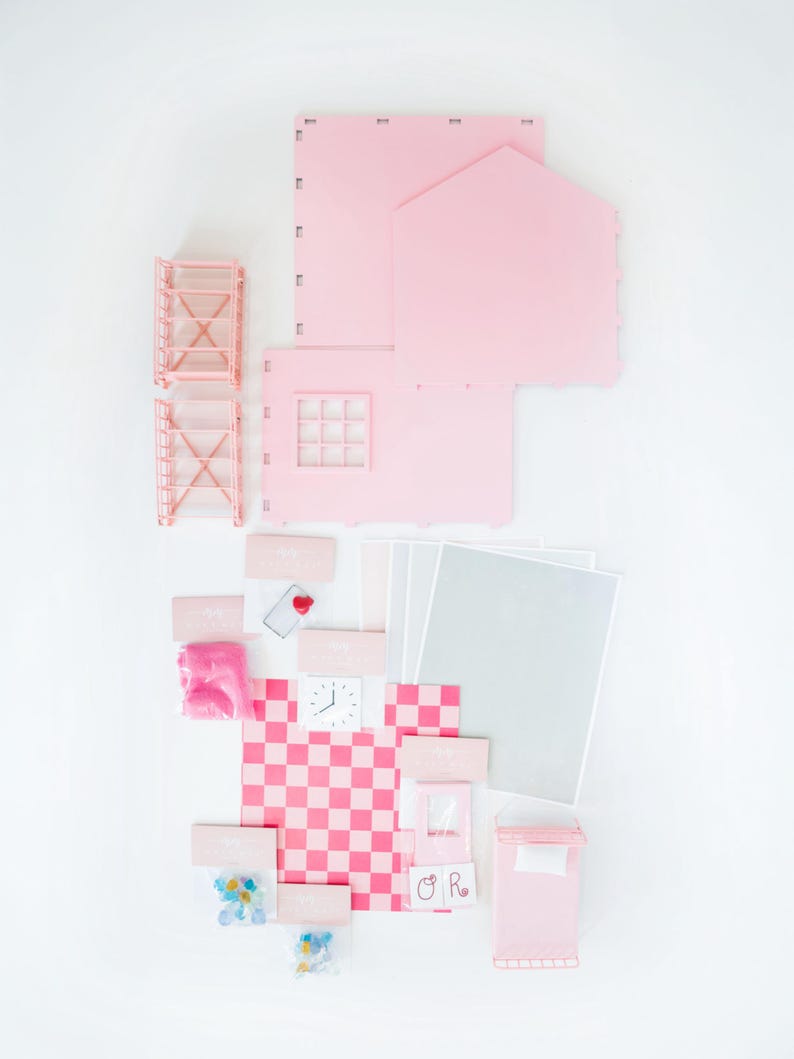 May include: A disassembled pink dollhouse kit with various components, including walls, a roof, and furniture. The kit includes a checkered floor, a clock, and small accessories. The pieces are arranged on a white surface.