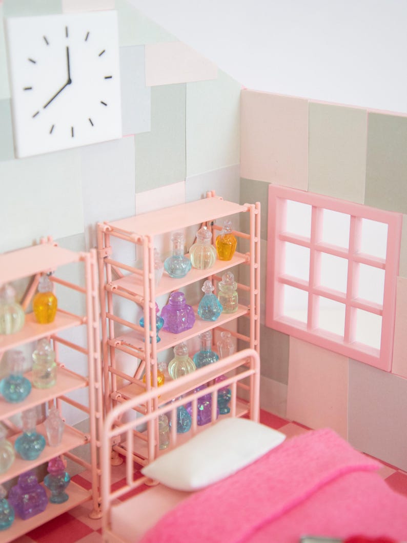 May include: A miniature bedroom scene with pink furniture, including a bed with a pink blanket and a shelf unit filled with colorful glass bottles. A white clock hangs on the wall. The room has a window and is decorated in pastel colors.
