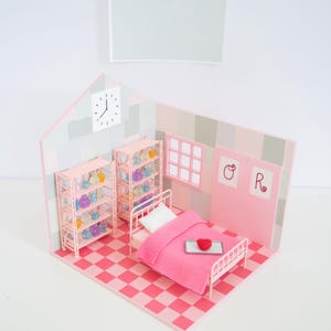 May include: A miniature pink bedroom scene with a bed, shelves, and a checkered floor. The bed has a pink blanket and a heart-shaped object on a tray. Shelves are filled with colorful objects. A clock is on the wall.