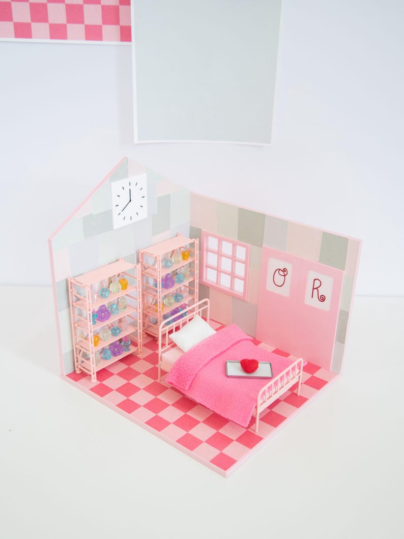 May include: A miniature pink bedroom scene with a bed, shelves, and a checkered floor. The bed has a pink blanket and a heart-shaped object on a tray. Shelves are filled with colorful objects. A clock is on the wall.