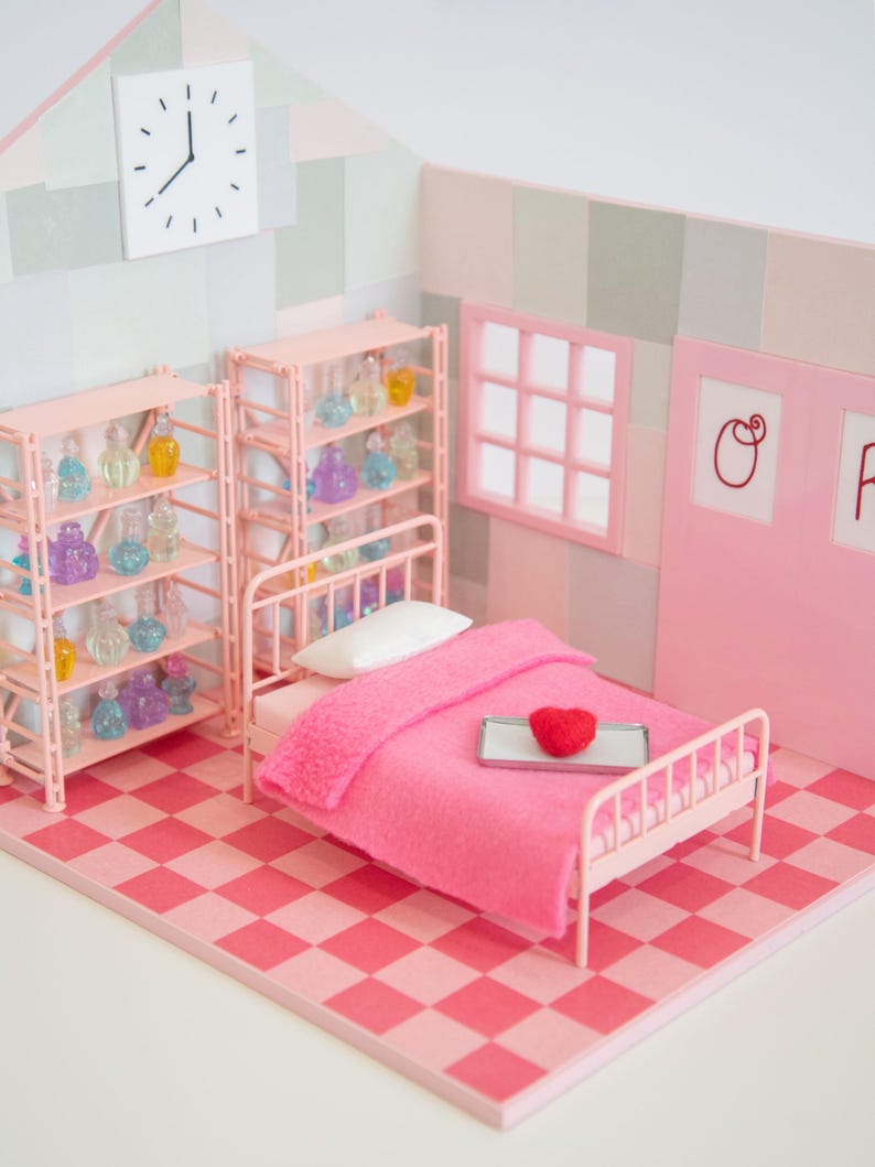 May include: A miniature pink bedroom scene with a bed, shelves, and a clock. The bed has a pink blanket and a red heart on a tray. Shelves display colorful bottles. The floor is a pink and red checkerboard pattern.