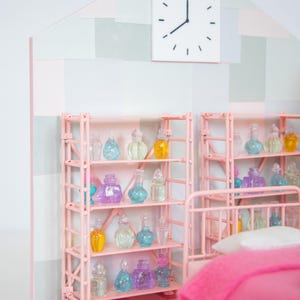 May include: A miniature dollhouse bedroom with pink shelving units filled with colorful glass bottles. A white clock hangs on the wall above the shelves. The room has a pink and white checkered floor and a pink bed with a pink blanket.