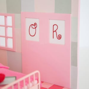May include: A miniature pink bedroom scene with a bed, window, and a door with the letters "O" and "R" in red. The floor has a pink and red checkered pattern, and the walls are a mix of pink and gray.