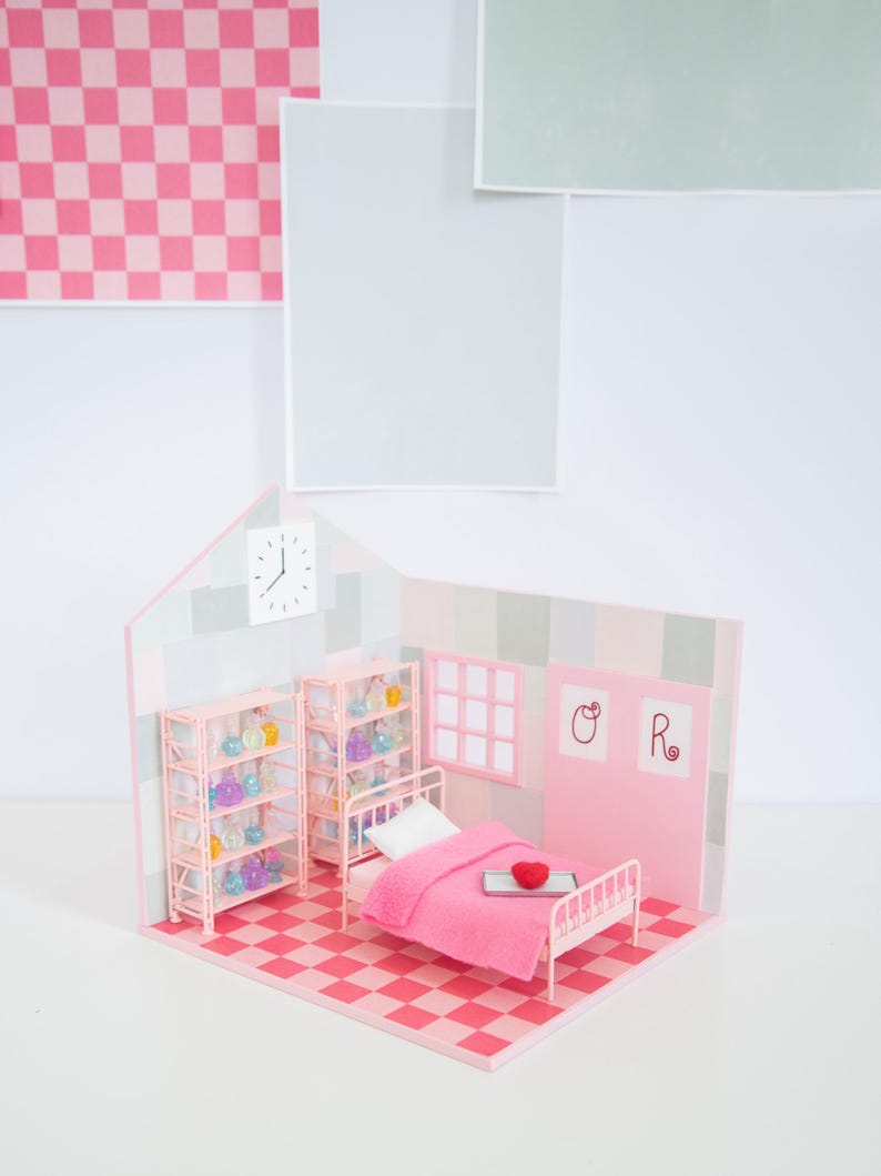 May include: A miniature pink bedroom scene with a bed, shelves, and a checkered floor. The bed has a pink blanket and a heart-shaped pillow. Shelves display colorful glass bottles. The walls are pink and gray, with a clock and artwork.