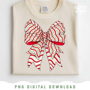 May include: Cream-colored sweatshirt featuring a large, festive bow design. The bow is red with white stripes and green accents, creating a candy cane-like pattern. The words "CRAFT COVE" are in the upper right corner, and "PNG DIGITAL DOWNLOAD" is at the bottom.