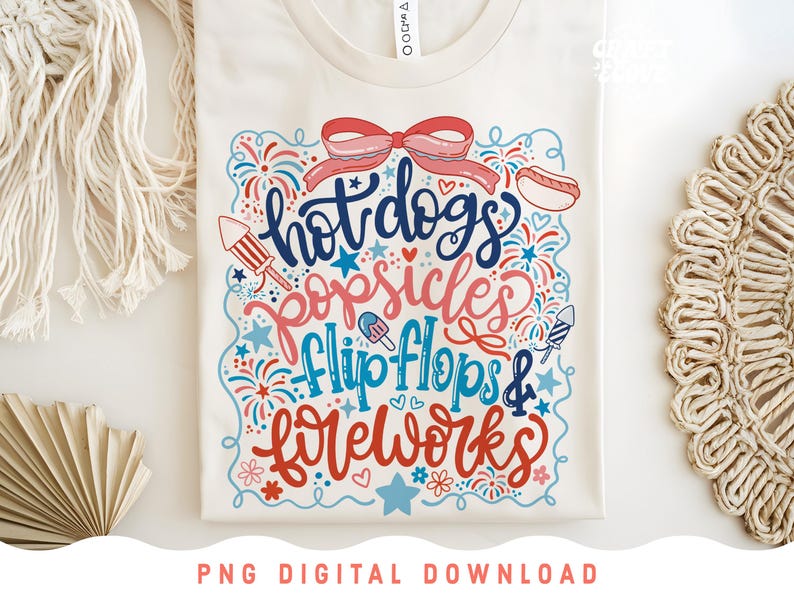 May include: Cream-colored t-shirt with a colorful graphic design. The design features the words "hot dogs, popsicles, flip flops & fireworks" in a playful font, along with illustrations of a hot dog, popsicle, fireworks, and a bow.