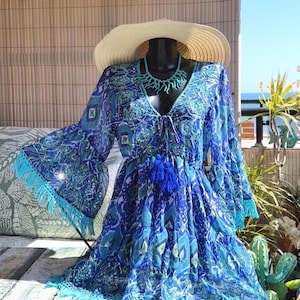 Peut inclure: Robe bleue à motifs avec manches longues évasées et jupe à volants. La robe présente une encolure en V avec une attache à pompon et est ornée de franges turquoise. Un chapeau de paille et un collier turquoise complètent l'ensemble.