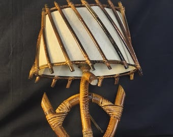 May include: A wall-mounted lamp featuring a curved bamboo frame shaped like an anchor. The lampshade is off-white and cylindrical, wrapped with diagonal bamboo slats that extend beyond the top and bottom edges of the shade structure.