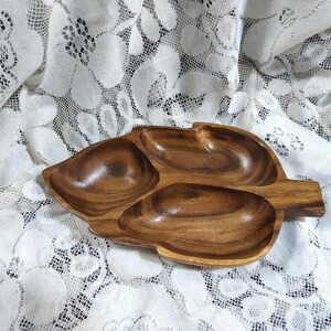 Peut inclure: Un plat de service en bois en forme de feuille avec trois compartiments. Le plat est fait d'un bois aux tons chauds avec des motifs de grain visibles. Les compartiments sont incurvés et lisses, parfaits pour servir des collations ou des apéritifs.