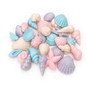 May include: A collection of small decorative seashells and a starfish in pastel shades of pink, blue, lavender, and cream. The items feature a pearlescent finish with various textures, including ribbed, spiral, and smooth surfaces, arranged in a cluster.