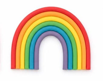 Puede incluir: Un objeto decorativo con forma de arcoíris compuesto por cinco tubos arqueados y lisos dispuestos en un patrón concéntrico. Los colores desde el arco exterior al interior son rojo, naranja, amarillo, verde, azul y morado, formando un arco.