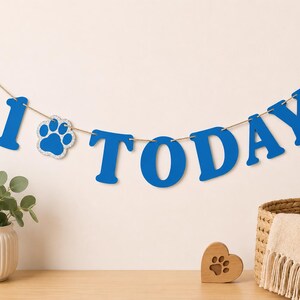 Puede incluir: Una pancarta azul que deletrea la palabra 1 TODAY con un icono de huella reemplazando la letra O. Las letras est&aacute;n ensartadas en un cordel marr&oacute;n fino. La pancarta presenta letras may&uacute;sculas en negrita de un color azul s&oacute;lido con acabado brillante.