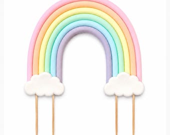 May include: A cake topper shaped like an arched rainbow with pastel bands of pink, orange, yellow, green, blue, and purple. Two white clouds are attached at the base of the rainbow, each supported by two thin, pointed wooden sticks for insertion.