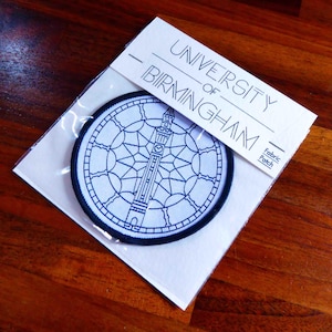 May include: A white fabric patch with black embroidery of the University of Birmingham clock tower. The text "University of Birmingham" is printed above the clock tower. The text "Fabric Patch" is printed in the bottom right corner.