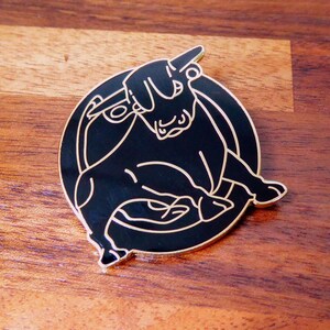 May include: Black and gold enamel pin featuring a stylised bull with its head turned to the side. The bull is outlined in gold and is set against a black background.