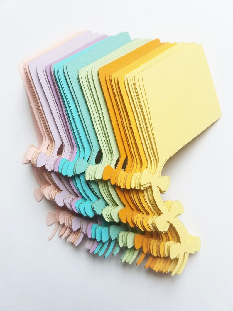 May include: A stack of colorful paper tags with a scalloped edge and a hole at the top. The tags are arranged in a rainbow pattern, starting with light pink and ending with yellow.