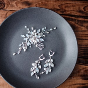 May include: A silver hair comb and earrings with delicate blue and white crystal accents on a gray plate.