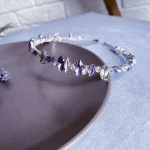 May include: A silver headband with purple and clear rhinestones. The headband is on a purple plate.
