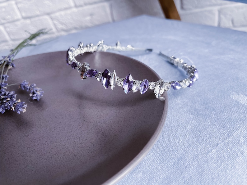 May include: A silver headband with purple and clear rhinestones. The headband is on a purple plate.