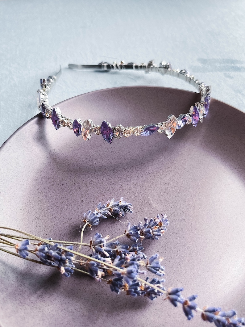 May include: A silver headband with a row of clear and purple rhinestones. The headband is on a purple plate with dried lavender flowers.
