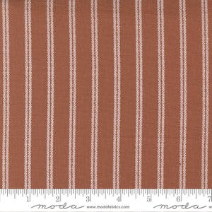 May include: A close-up of a rust-colored fabric with thin white stripes. The fabric is measured with a ruler in inches.