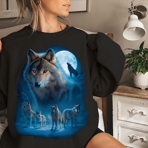 May include: Black sweatshirt with a striking wolf illustration. The design shows a wolf under a full moon, with other wolves in the foreground. The artwork uses blue and grey tones.