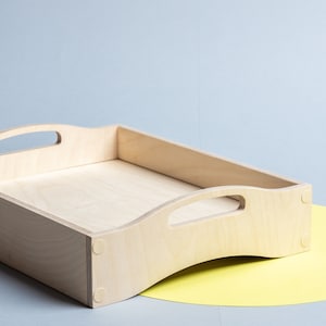 Può includere: Un vassoio da portata in legno chiaro con due manici. Il vassoio è appoggiato su un cerchio giallo.