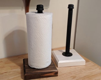 May include: Two black metal pipe paper towel holders. One is mounted on a dark wood base and the other is mounted on a white base.