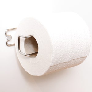 May include: A white toilet roll is mounted on a silver metal holder. The holder has a simple design with a curved arm and a round base.
