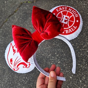 May include: White headband with a red velvet bow and two white ear pieces. One ear piece has a white embroidered image of a panther head and the other has a white embroidered basketball with the text "East High Basketball".
