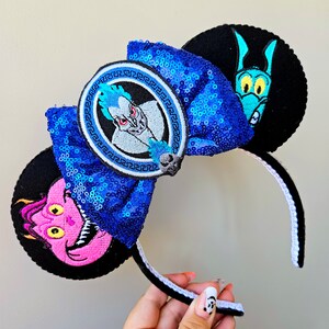 Puede incluir: Orejas de rat&oacute;n azules y negras con un lazo de lentejuelas azules. El lazo tiene un parche circular con un personaje de la pel&iacute;cula de Disney H&eacute;rcules. La otra oreja tiene un personaje en blanco y negro de la pel&iacute;cula de Disney La Sirenita.