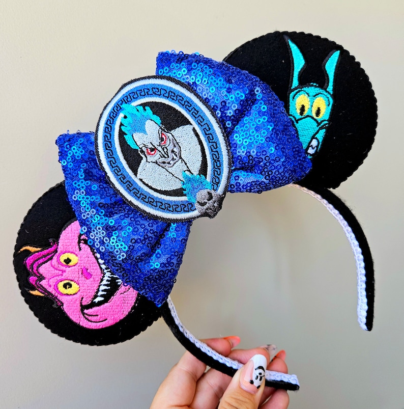 Puede incluir: Orejas de rat&oacute;n azules y negras con un lazo de lentejuelas azules. El lazo tiene un parche circular con un personaje de la pel&iacute;cula de Disney H&eacute;rcules. La otra oreja tiene un personaje en blanco y negro de la pel&iacute;cula de Disney La Sirenita.