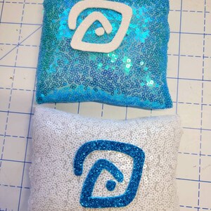 May include: Two decorative pillows with a blue and white geometric design. The pillows are covered in sequins and have a white background with a blue geometric design on one pillow and a blue background with a white geometric design on the other pillow.