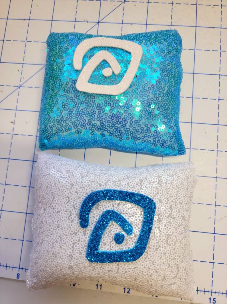 May include: Two decorative pillows with a blue and white geometric design. The pillows are covered in sequins and have a white background with a blue geometric design on one pillow and a blue background with a white geometric design on the other pillow.