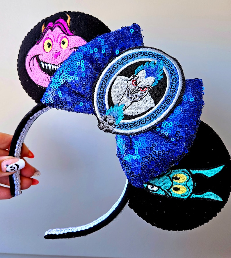 Puede incluir: Diadema azul y negra con un lazo de lentejuelas azules y tres parches bordados con personajes de H&eacute;rcules de Disney. Los parches incluyen a Hades, Dolor y P&aacute;nico.
