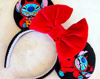 May include: Black and red Mickey Mouse ears with a red velvet bow. The ears feature an embroidered image of Stitch dressed as a devil holding a jack-o-lantern.
