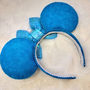 May include: Blue fabric mouse ears with a sparkly blue bow. The headband is white with a blue trim.