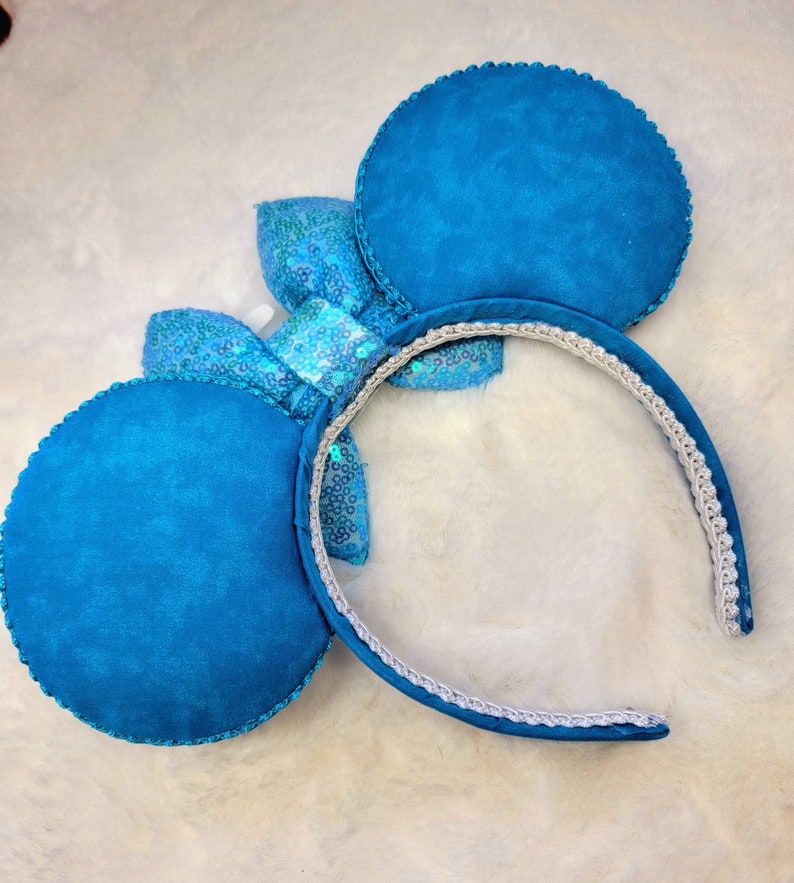 May include: Blue fabric mouse ears with a sparkly blue bow. The headband is white with a blue trim.