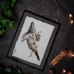 Puede incluir: Una ilustración enmarcada en blanco y negro de una ballena con una cuerda dorada envuelta a su alrededor. La ballena sostiene una pequeña maceta con una planta que crece fuera de ella. La ilustración está sobre un fondo blanco.