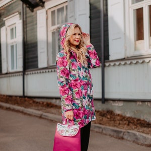 May include: A woman wearing a pink floral print raincoat with a hood and black pants. She is carrying a pink backpack with a floral print.