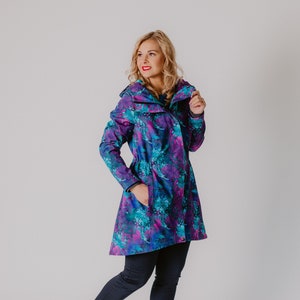 May include: A woman wearing a long, blue and purple floral print jacket with a hood. She is wearing black pants and white sneakers.