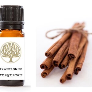 Può includere: Una bottiglia di vetro marrone con un tappo nero e un'etichetta bianca. L'etichetta presenta un disegno di albero dorato e il testo "Cinnamon Fragrance". È mostrato anche un mazzo di bastoncini di cannella.