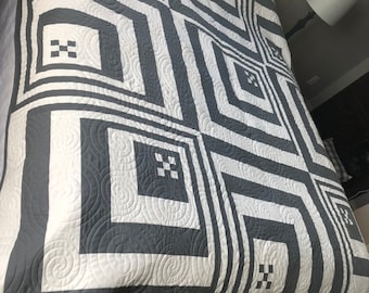 Puede incluir: Una colcha blanca y gris con un patrón geométrico de cuadrados y espirales. La colcha está hecha con una tela suave acolchada y tiene un diseño moderno.