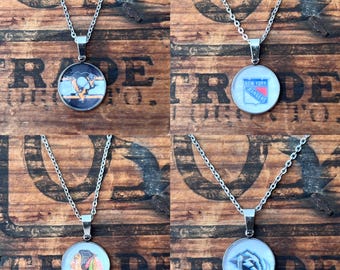 May include: Four silver-toned necklaces with round pendants featuring hockey team logos. The logos include the Pittsburgh Penguins, New York Rangers, Chicago Blackhawks, and San Jose Sharks. The pendants are attached to delicate chain necklaces.