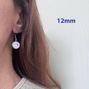May include: A silver-toned drop earring featuring a circular charm with the Toronto Blue Jays logo, which includes a blue bird and a red maple leaf. The charm has a diameter of 12mm and hangs from a simple silver-toned hook wire.