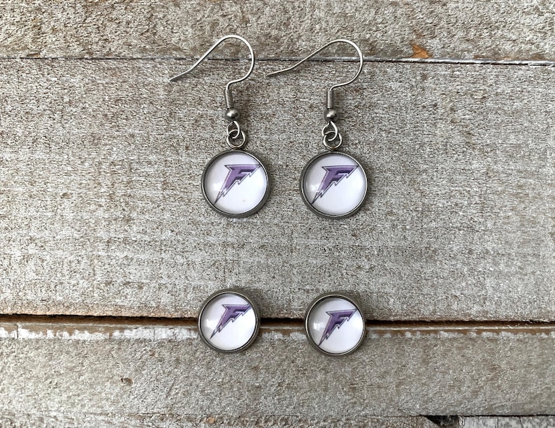 May include: A pair of silver-toned drop earrings and a pair of matching stud earrings. Each piece features a circular setting with a white background and a purple letter F graphic with a lightning bolt design integrated into the letter's shape.